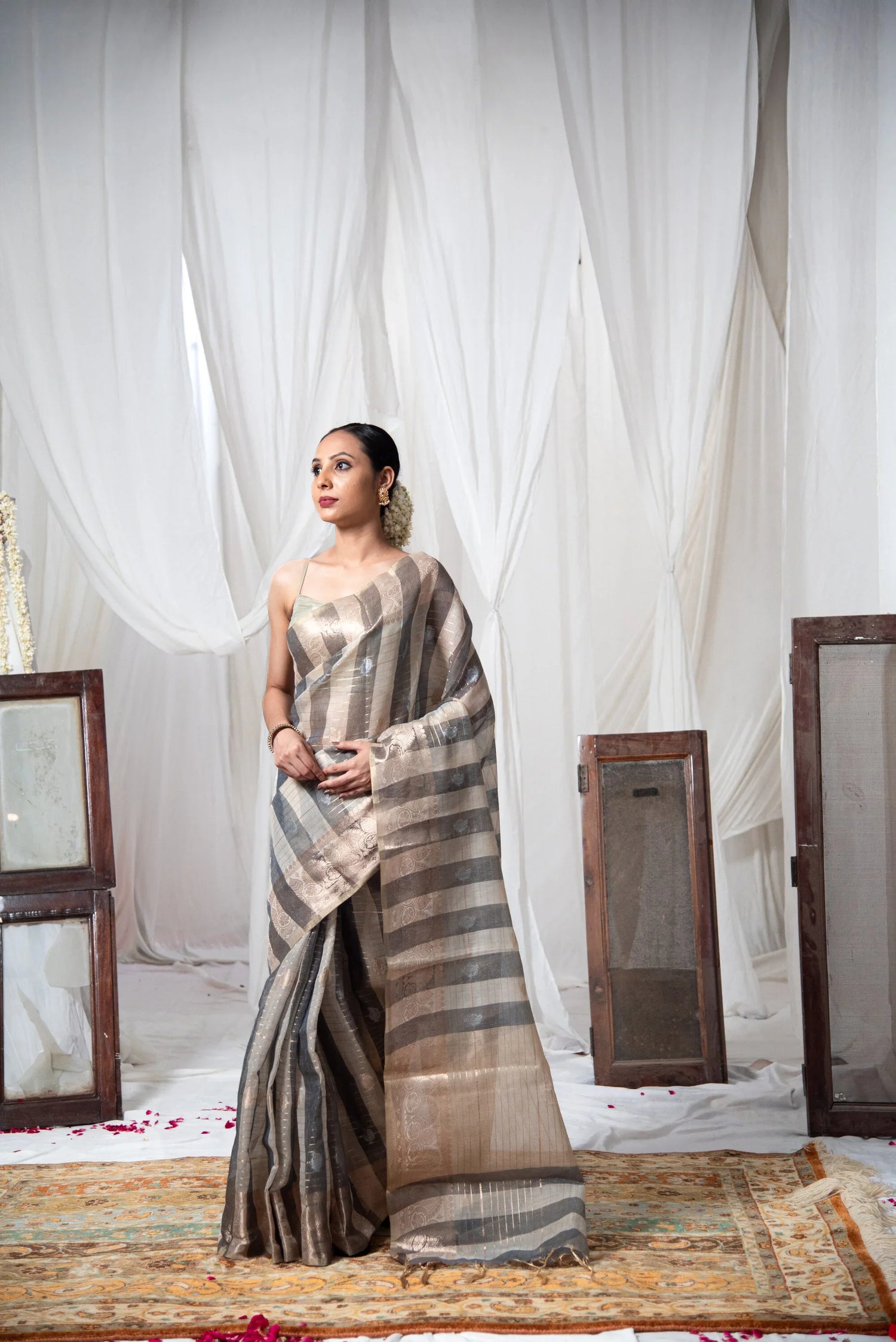 Woman wearing striped Banarasi cotton linen saree in a minimal indoor setting with white drapes