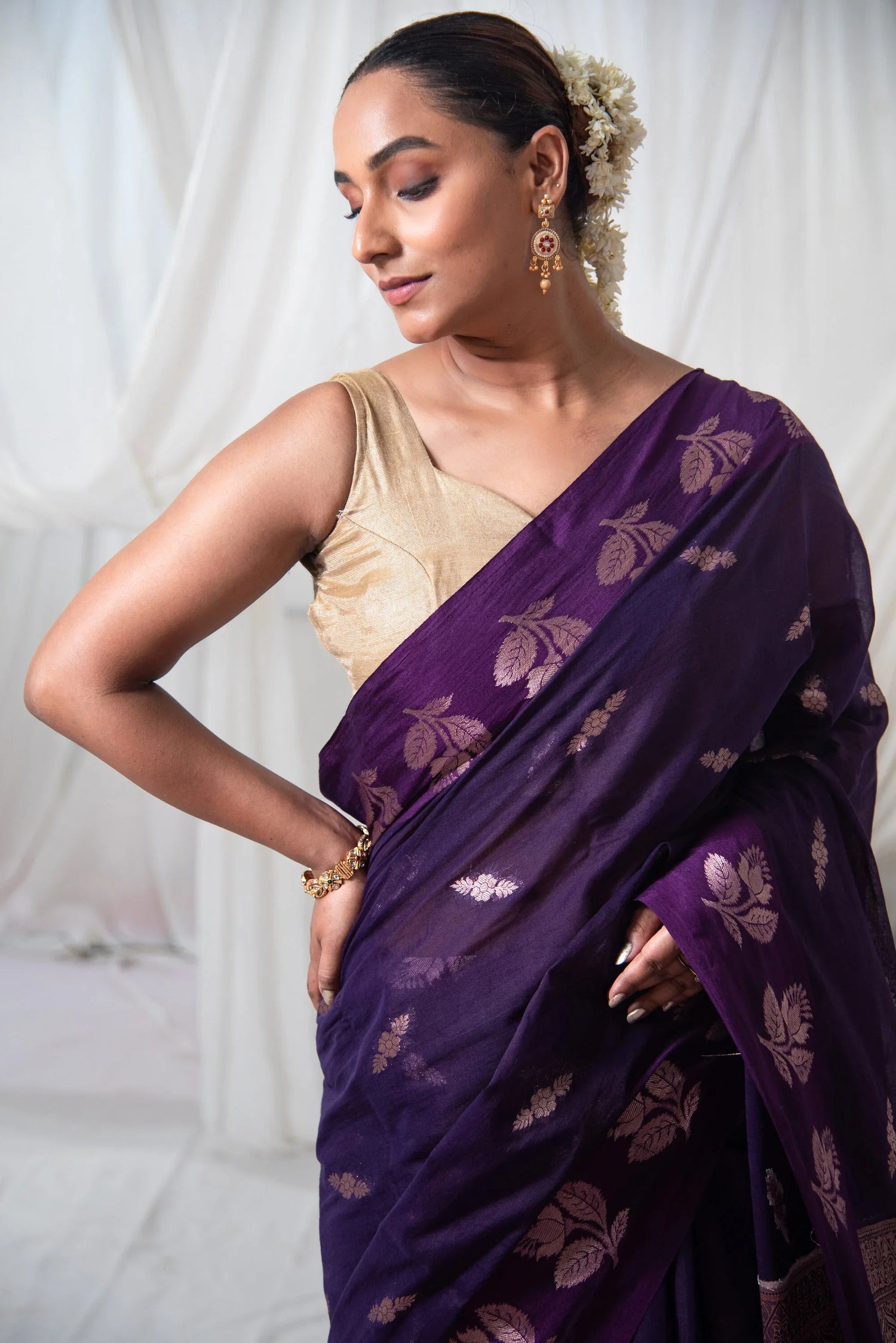 Woman in a purple Banarasi cotton saree with gold floral motifs and traditional jewelry