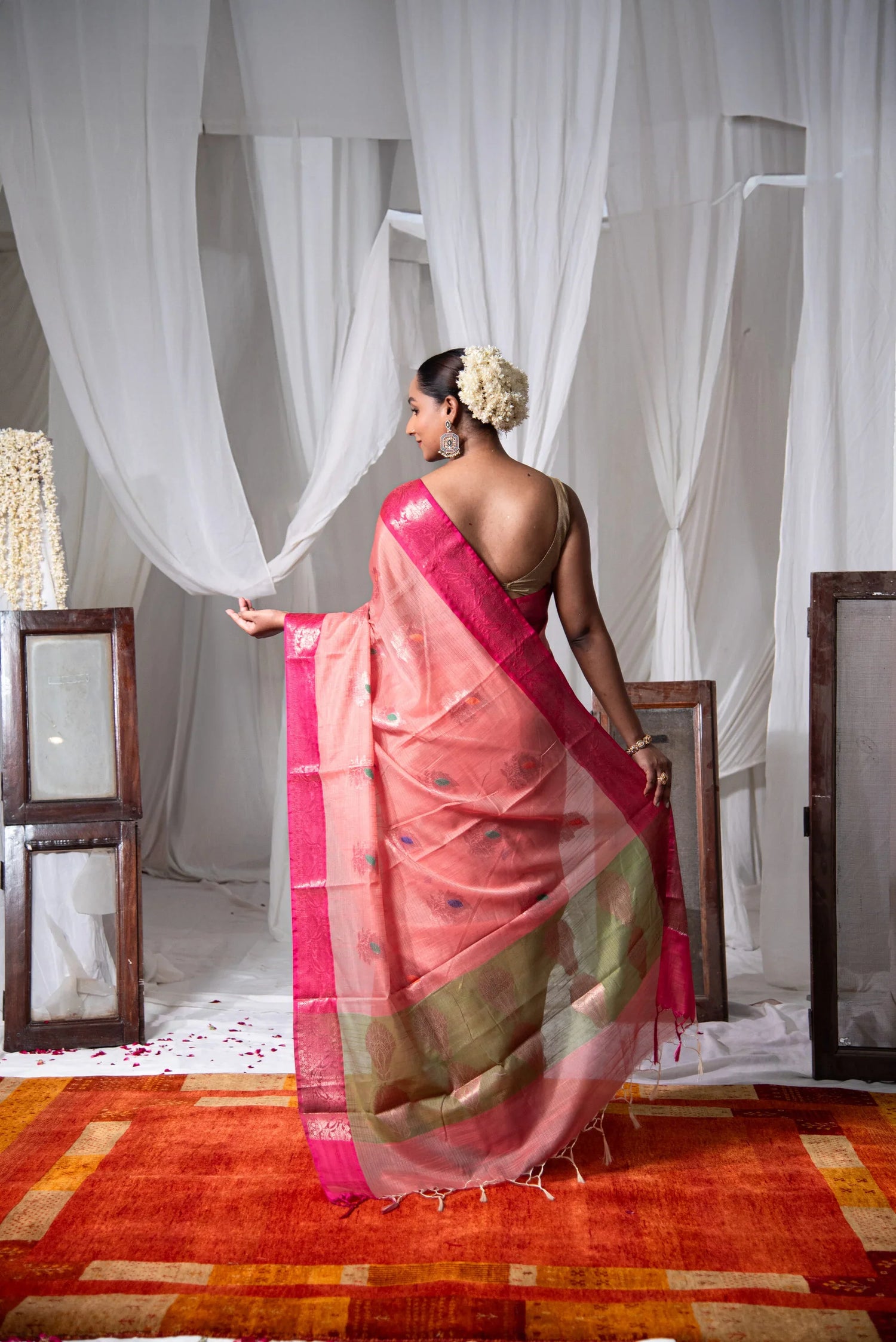 Woman in a pink dual-tone Banarasi cotton saree with tassels, standing on a red carpet.
