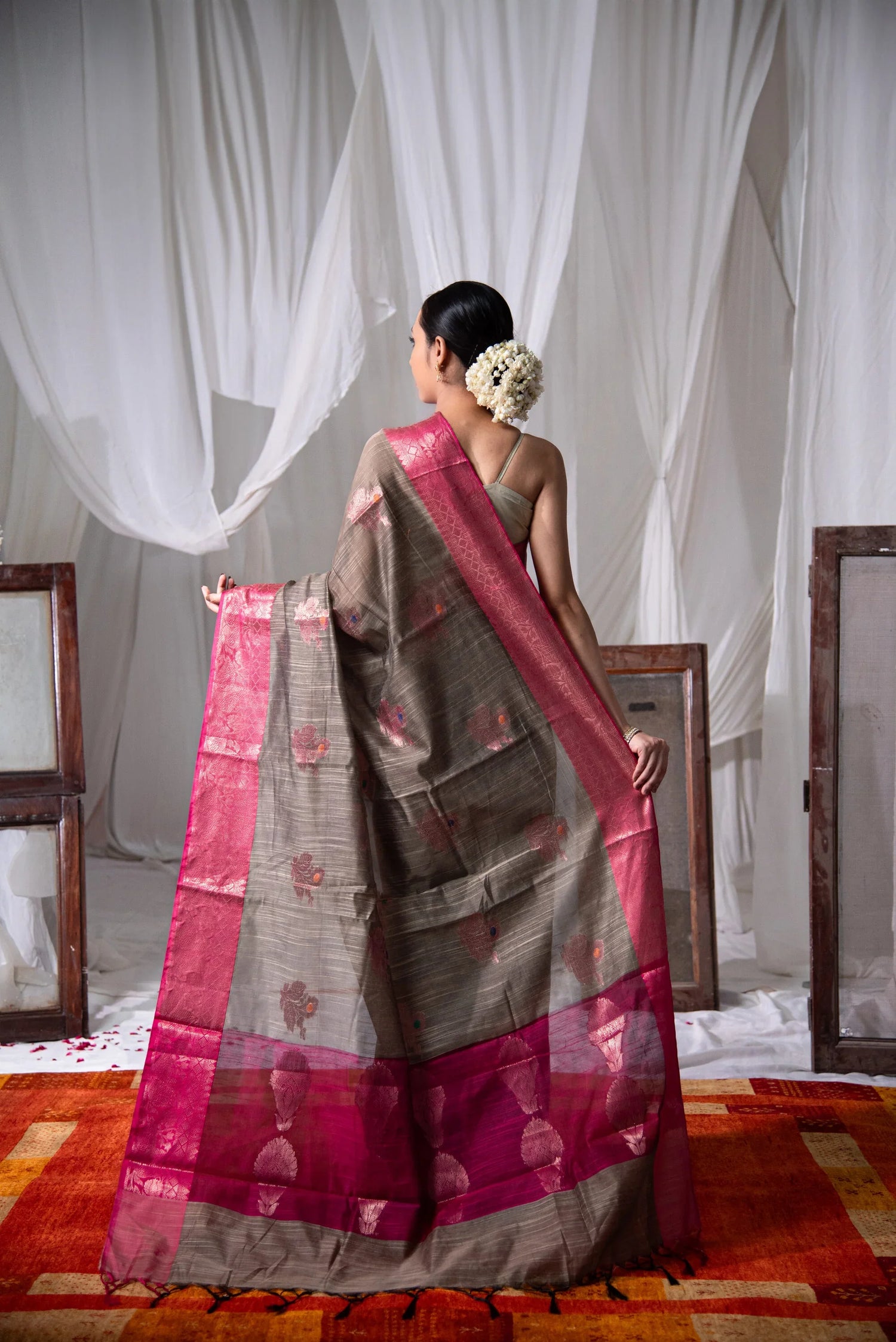 Woman wearing Banarasi cotton saree with red border and floral motifs, viewed from back