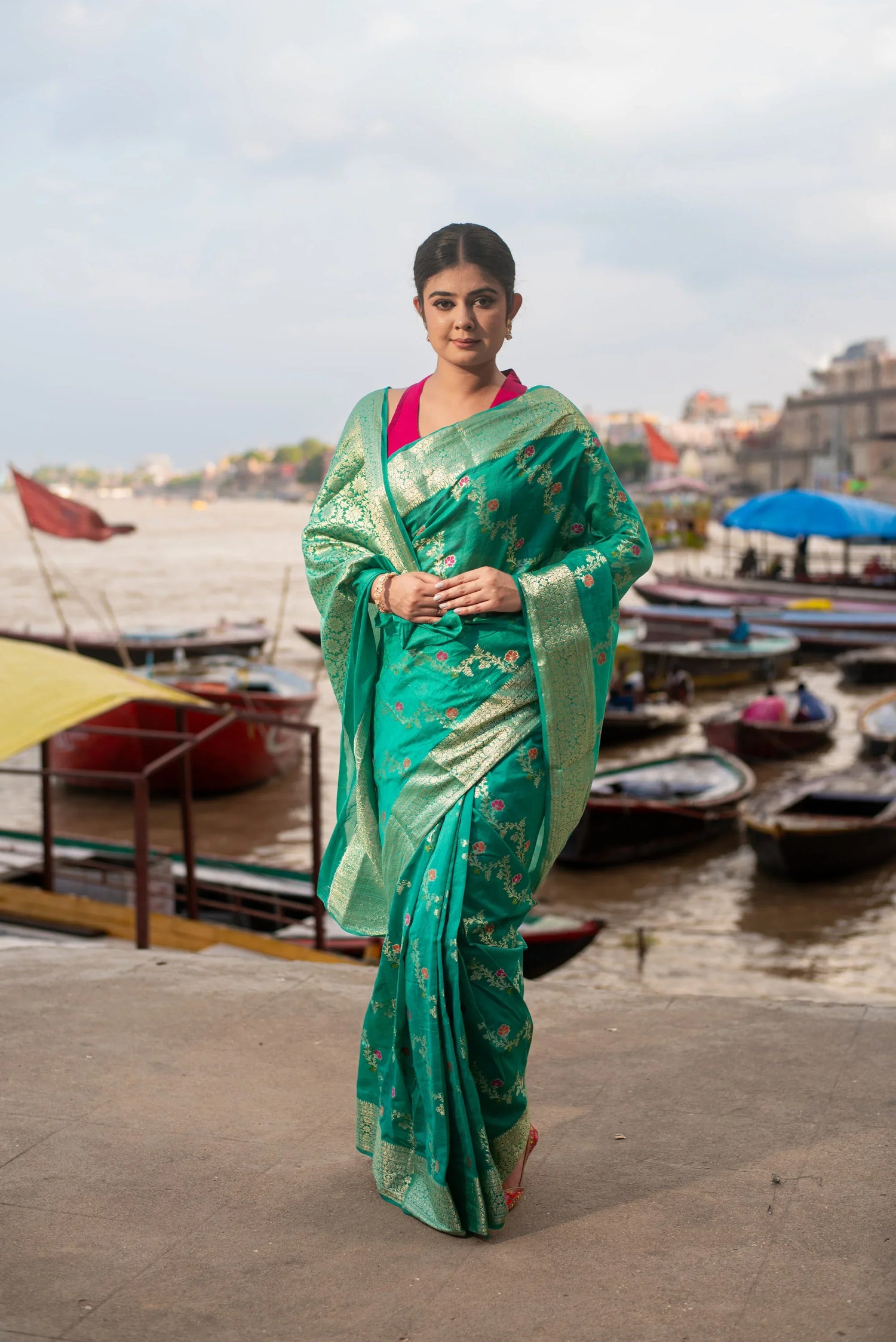 Woman in green Banarasi silk saree with Meenakari work by riverside with boats in background