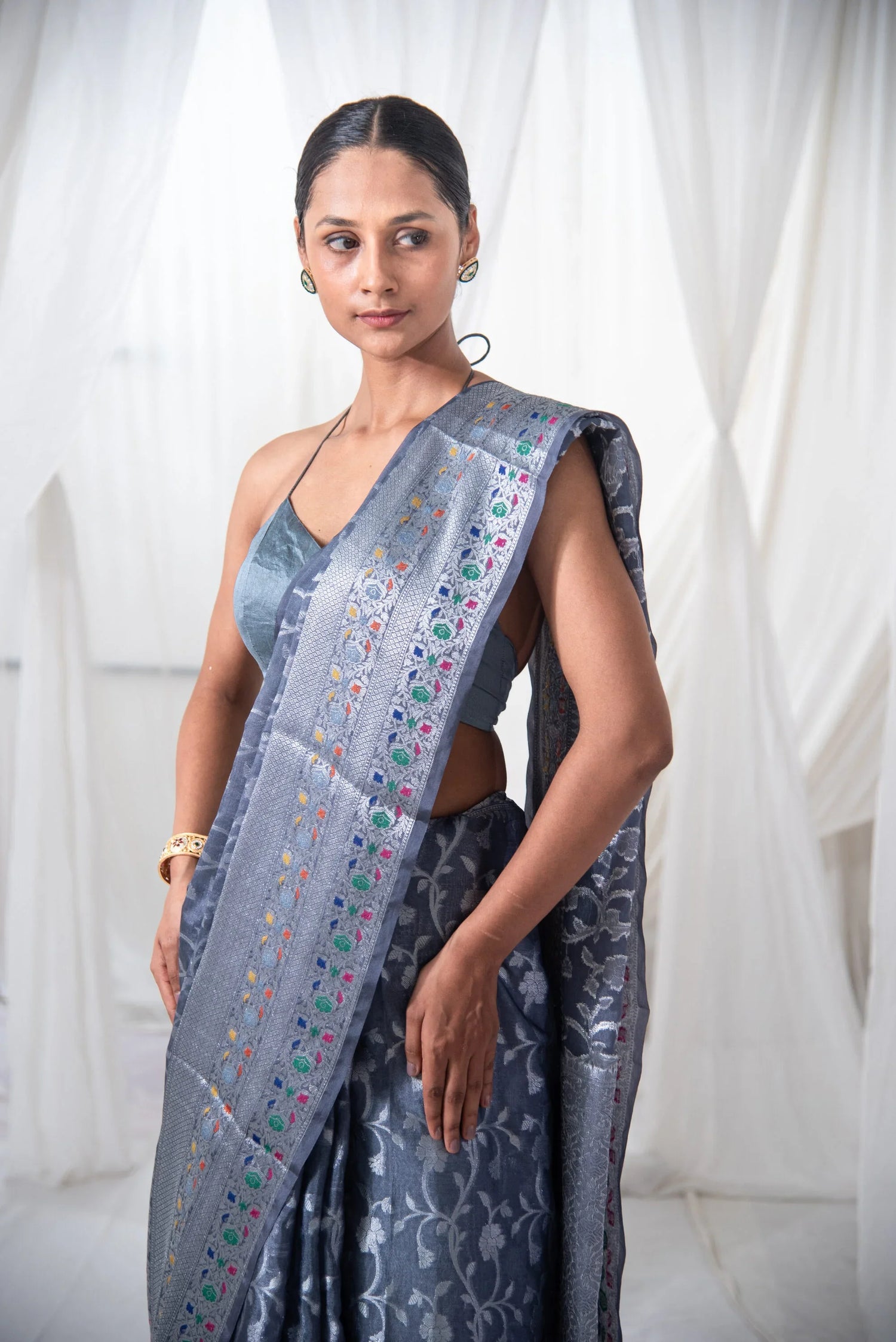 Woman wearing a silver Banarasi silk saree with floral motifs and colorful border