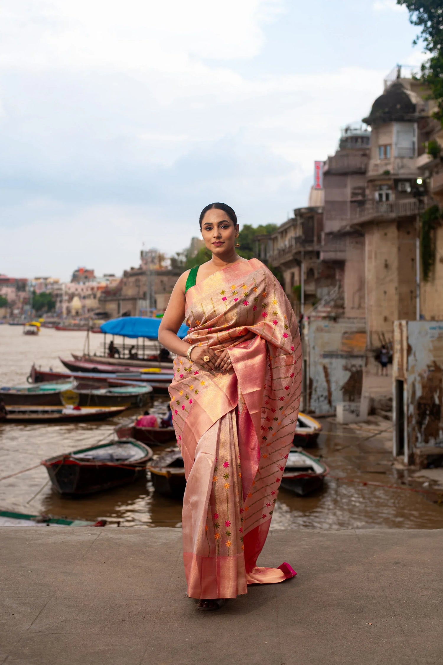 Woman in pink Banarasi tissue saree with Meenakari work by riverside with boats and ghats