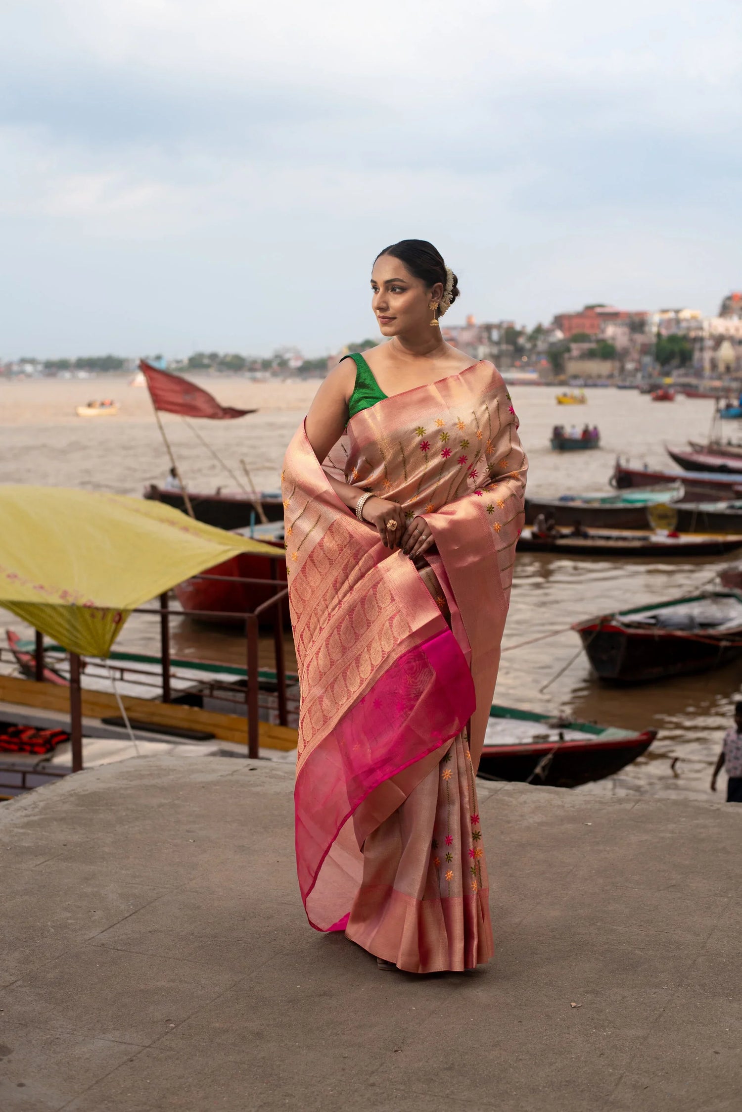 Woman in pink Banarasi silk saree with floral meenakari design by riverside with boats