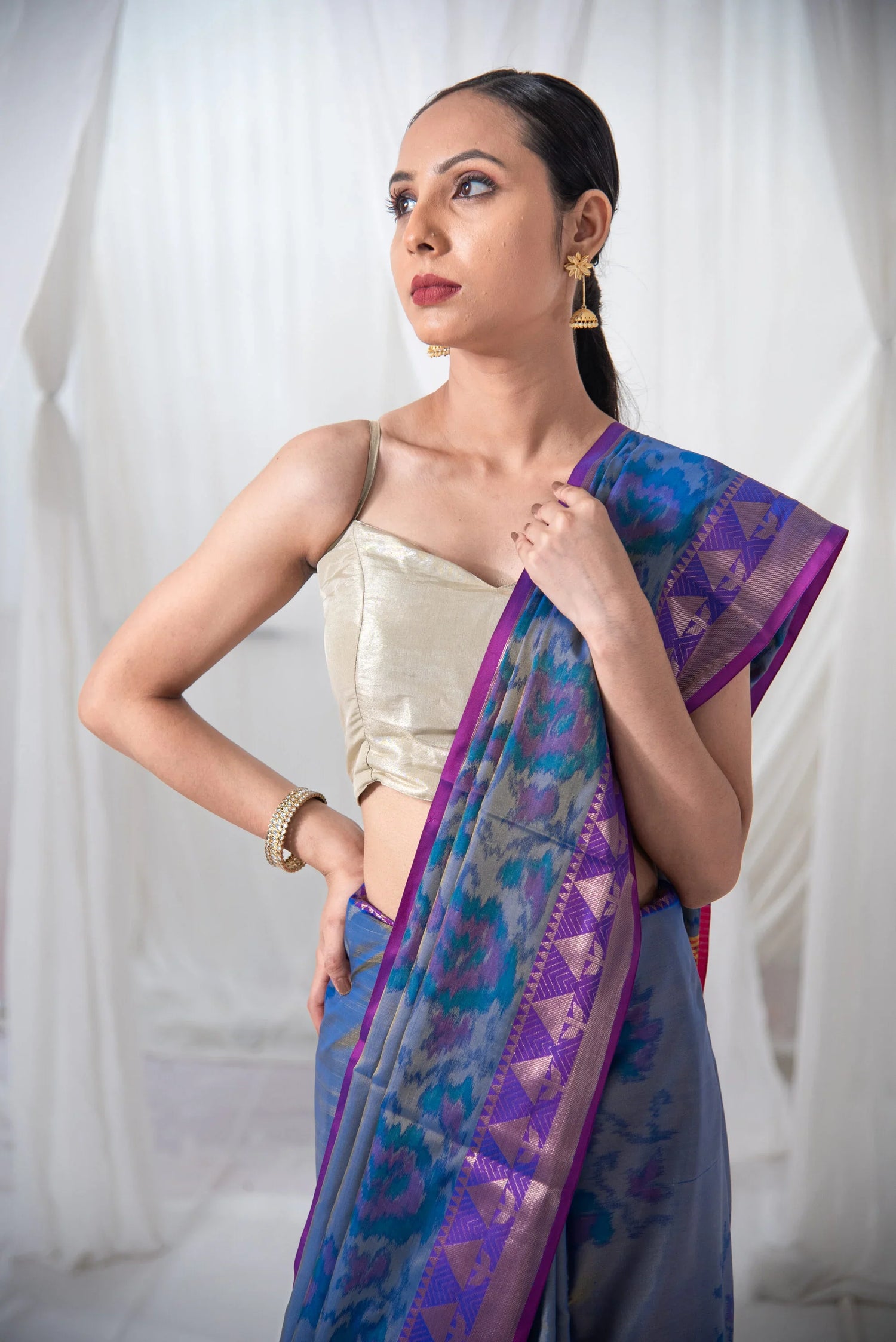 Woman wearing blue and purple Ikkat silk saree with gold blouse, traditional jewelry