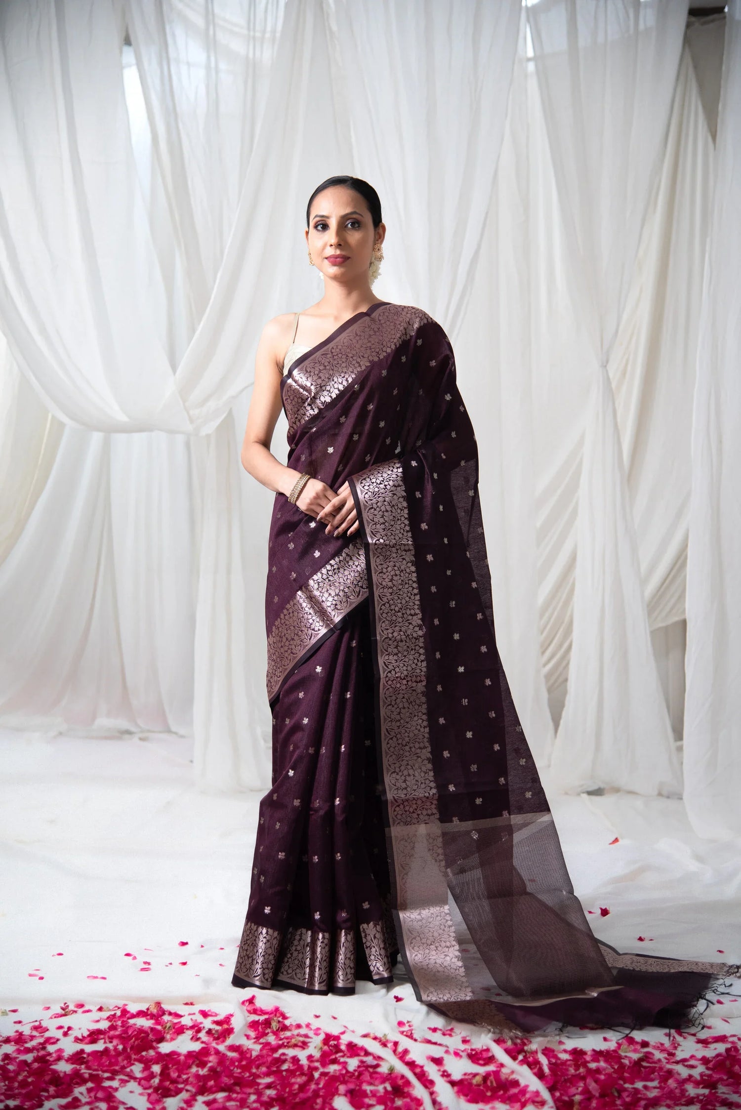 Woman wearing maroon Banarasi cotton saree with zari border, standing on rose petals