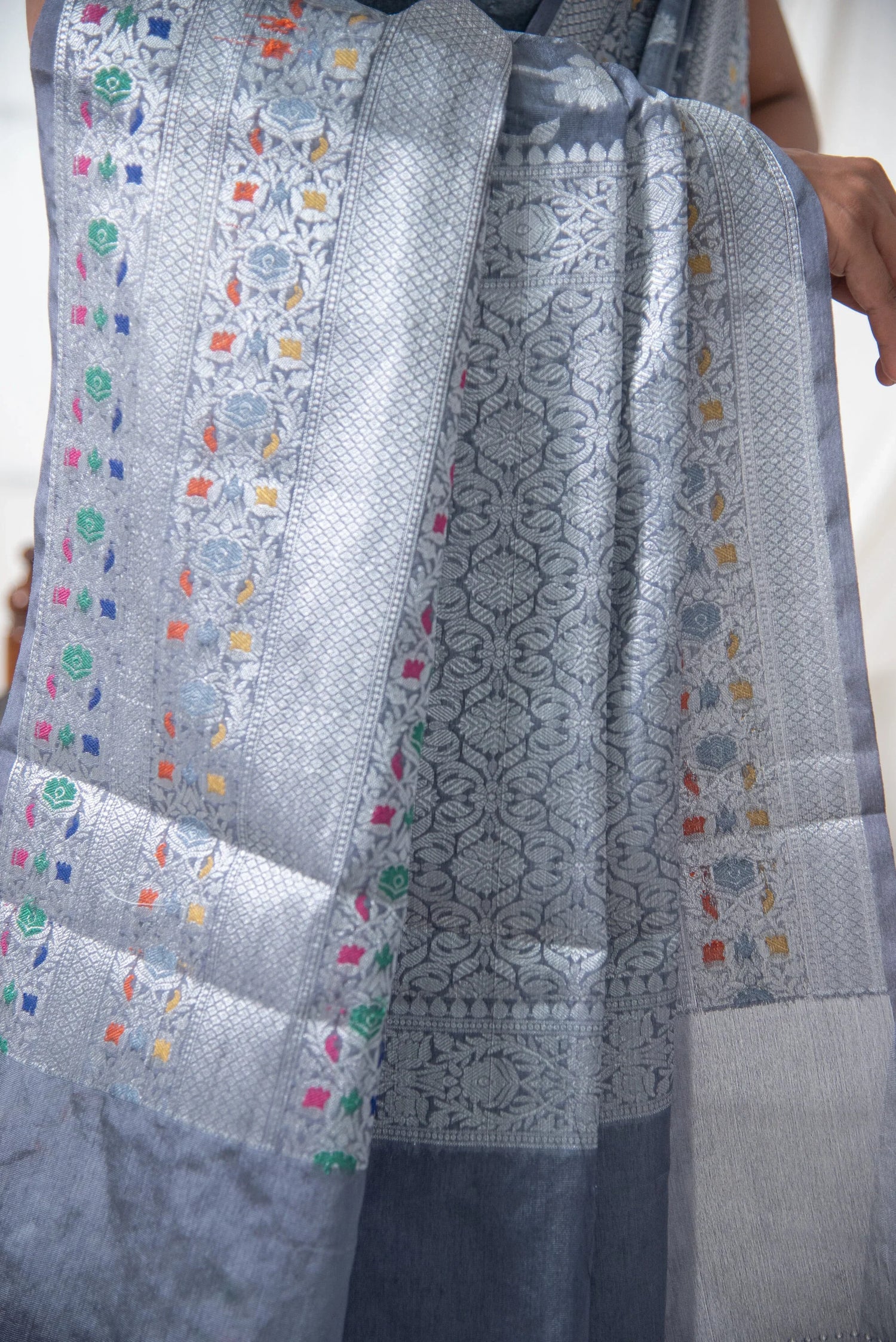 Silver Banarasi silk saree with intricate floral patterns and colorful woven accents