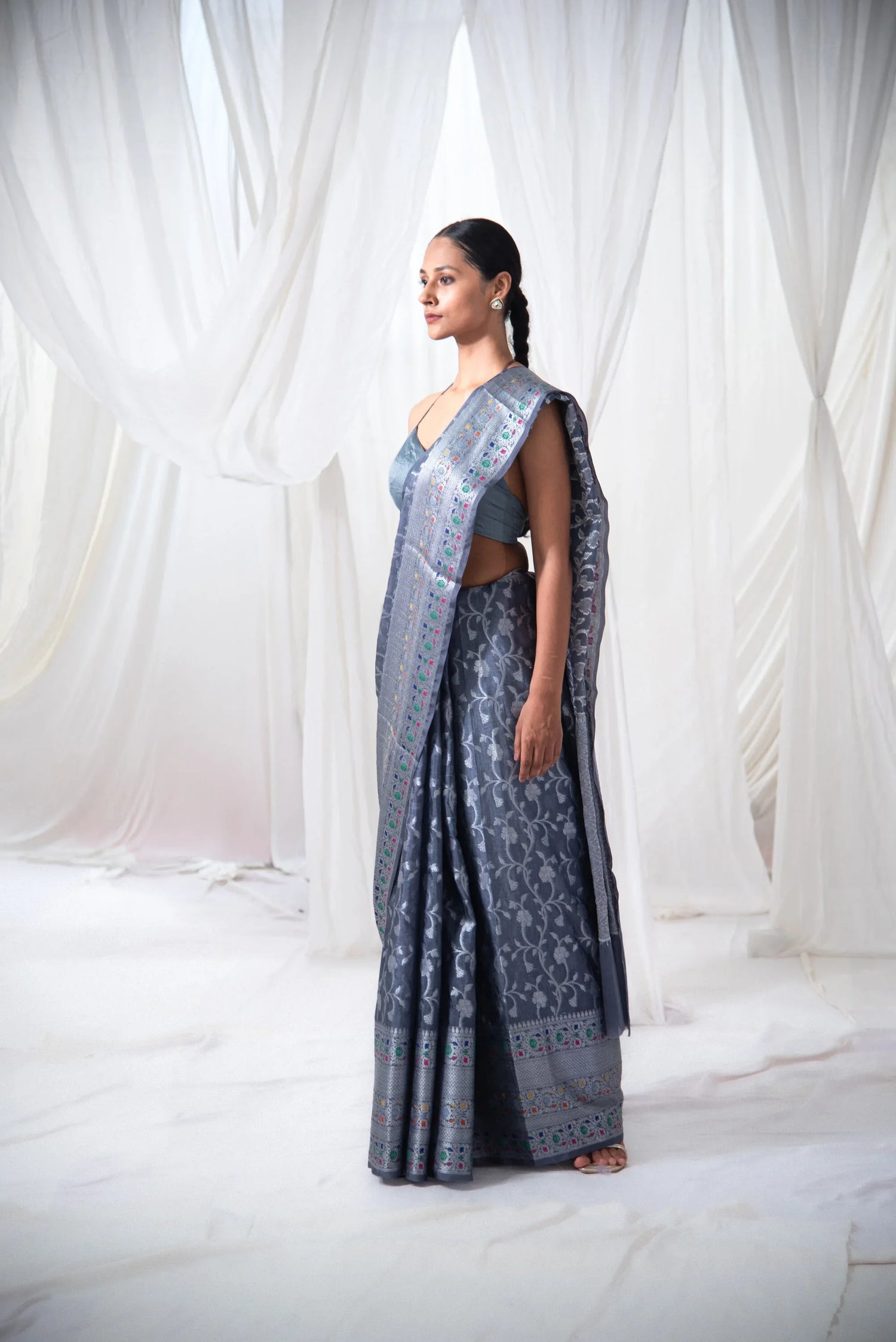 Woman wearing a blue Banarasi silk saree with floral motifs and intricate border, standing indoors