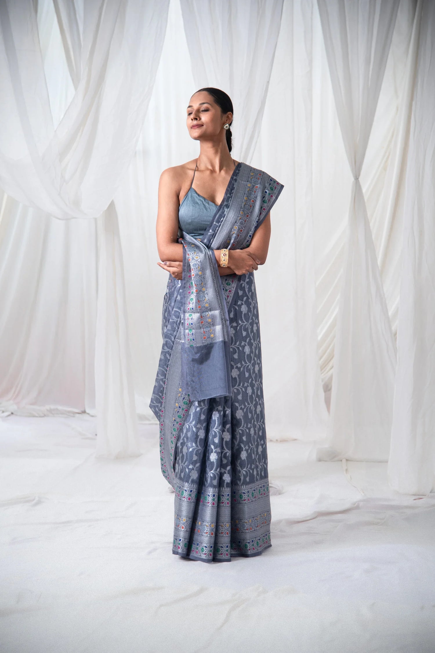 Woman wearing a grey Banarasi silk saree with intricate woven patterns in a white draped setting