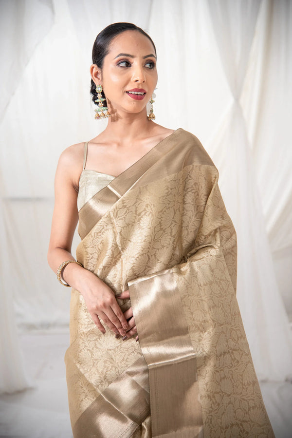 Woman wearing gold Banarasi silk saree with floral pattern in elegant indoor setting