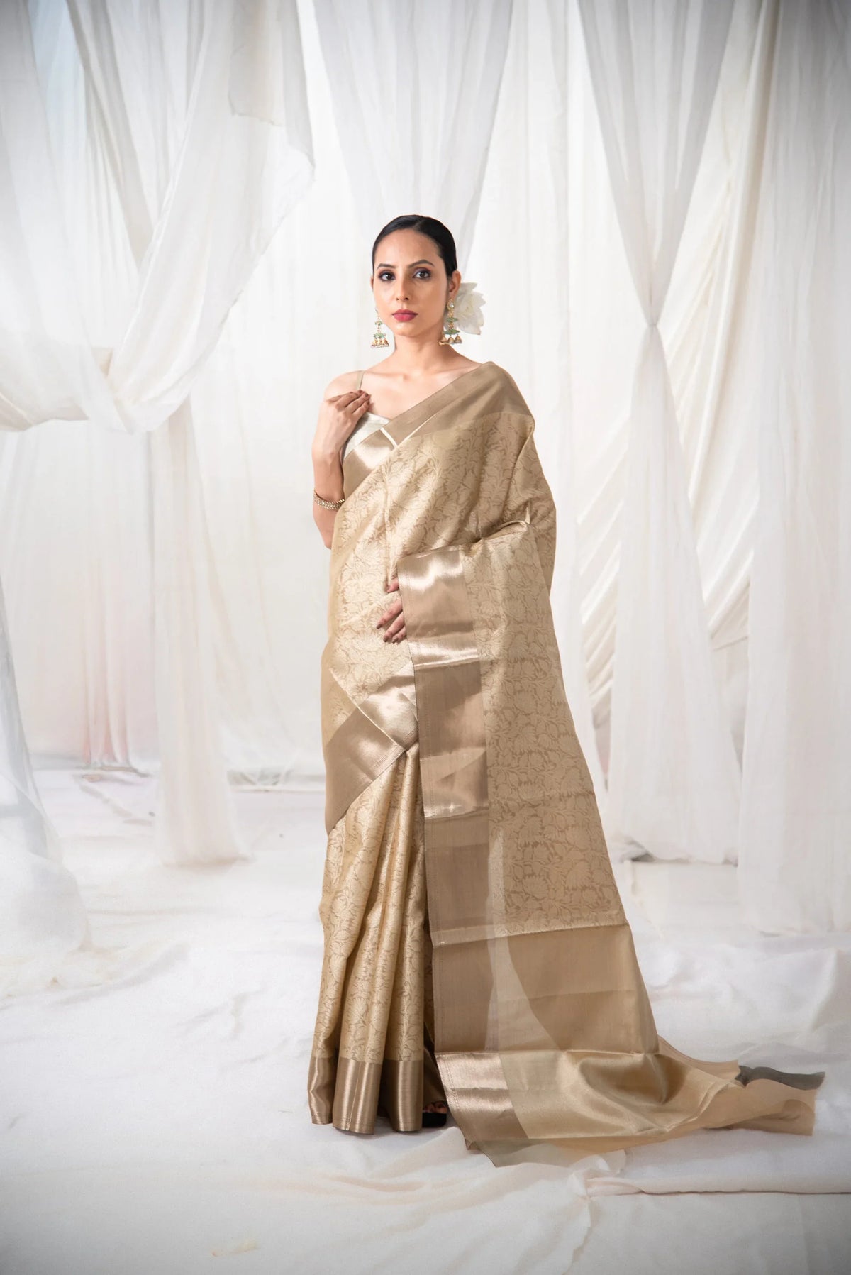 Woman wearing gold Banarasi tissue silk saree with floral design in a white draped setting