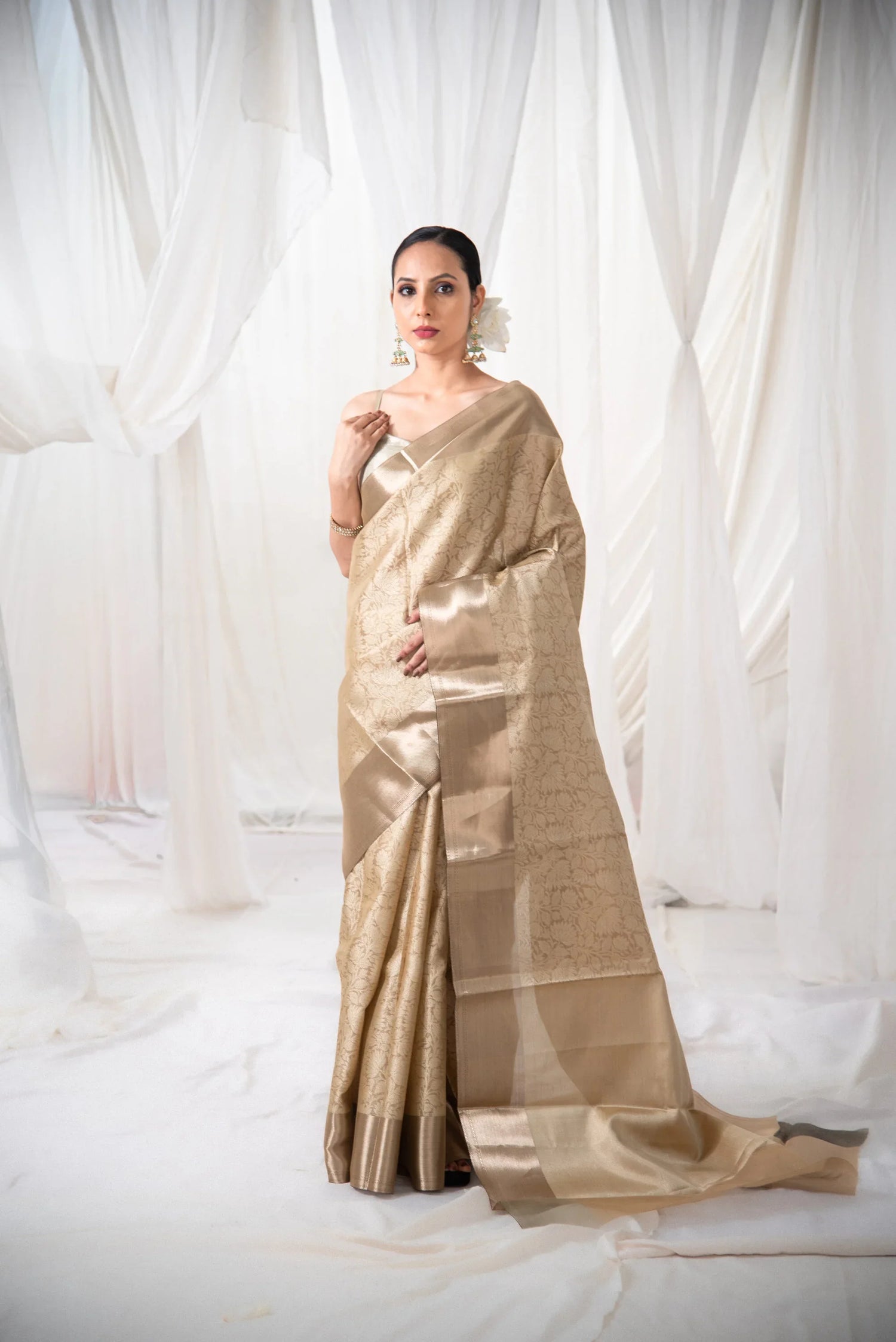 Woman wearing gold Banarasi tissue silk saree with floral design in a white draped setting