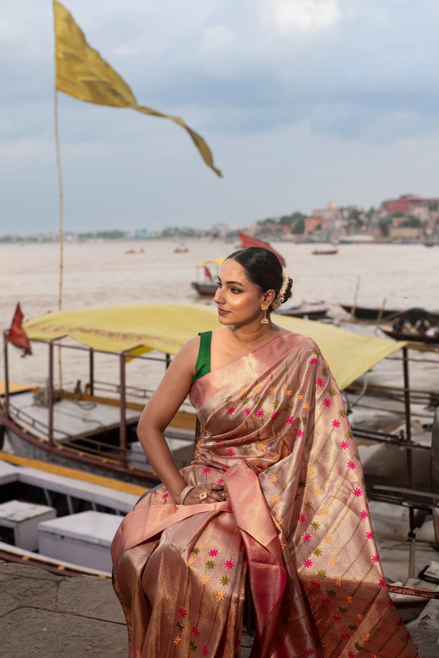 Woman in gold Banarasi silk saree with floral Meenakari design by riverside boats