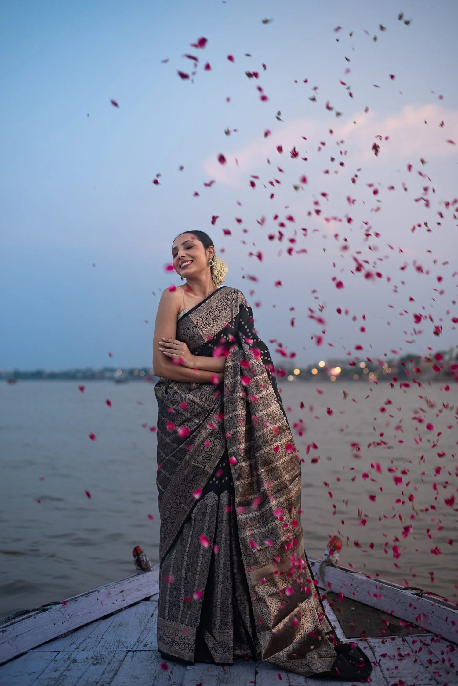 Woman wearing Banarasi Katan silk saree with zari work by riverside with rose petals falling