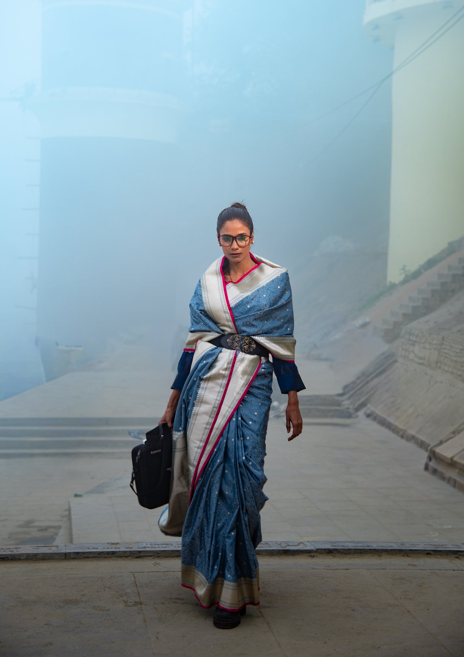 Woman wearing blue Banarasi Tanchui Mashru silk saree with peacock detailing in outdoor architectural setting, pre-draped saree showing complete styling with white blouse and accessories